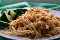 Long and wide pasta spaghetti noodles under viscous melted cheese on a platter with sliced Ã¢â¬â¹Ã¢â¬â¹fresh cucumbers on a bright green